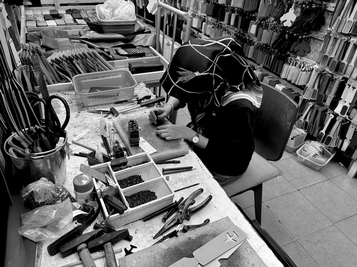 A woman with a headscarf on a workbench working on leather.