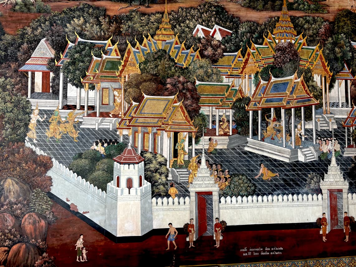 A colorful mural depicts a traditional Thai scene with ornate temples, buildings, and figures within walled courtyards, set against a backdrop of trees.