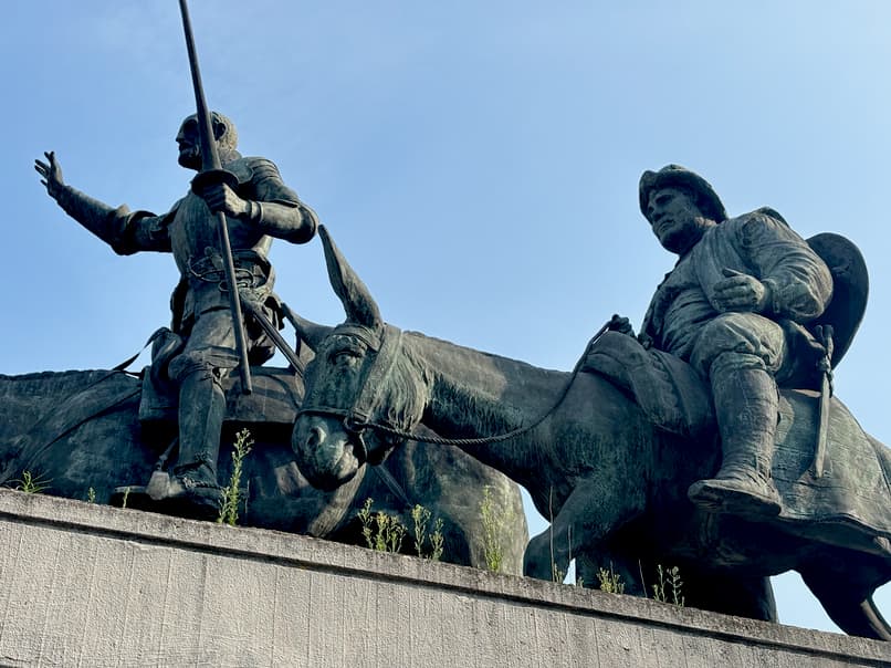 A statue of Don Quixote on a horse and Sancho Panza on a donkey, seen from a low angle against a clear sky.
