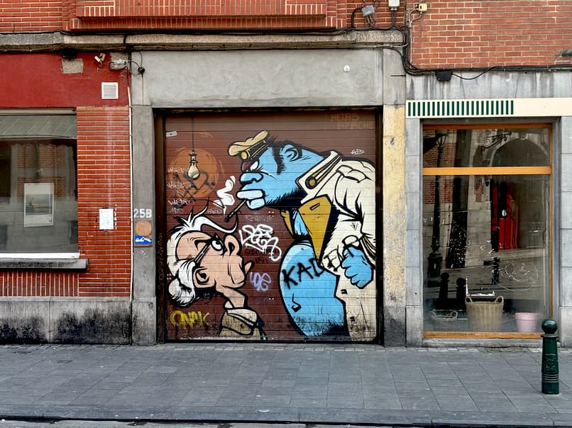 A street-level photo showing a garage door with a colorful cartoon mural featuring two characters, one smoking a cigarette.