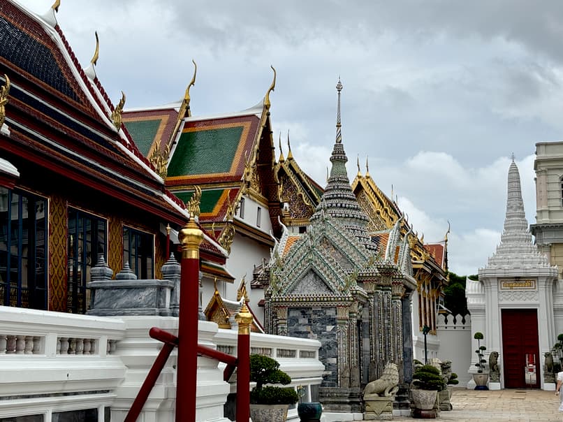 Ornate rooftops and spires of the Grand Palace in Bangkok, Thailand, under a cloudy sky.