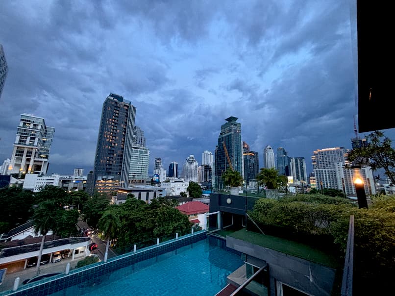 Thonglor Bangkok skyline at dusk with high-rise buildings and a rooftop pool under dramatic, cloudy skies.