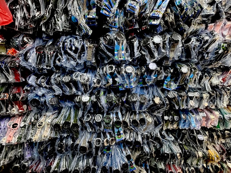 Hundreds of individually plastic-wrapped watches, mostly dark and varied in design, are densely displayed.