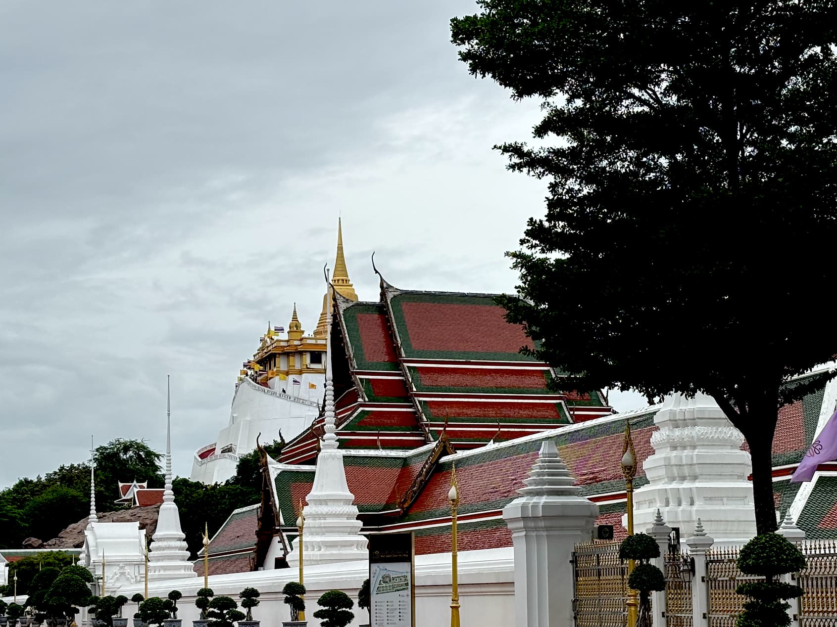 View of Wat Saket and the Golden Mount in Bangkok, with temple rooftops and white stupas in the foreground.